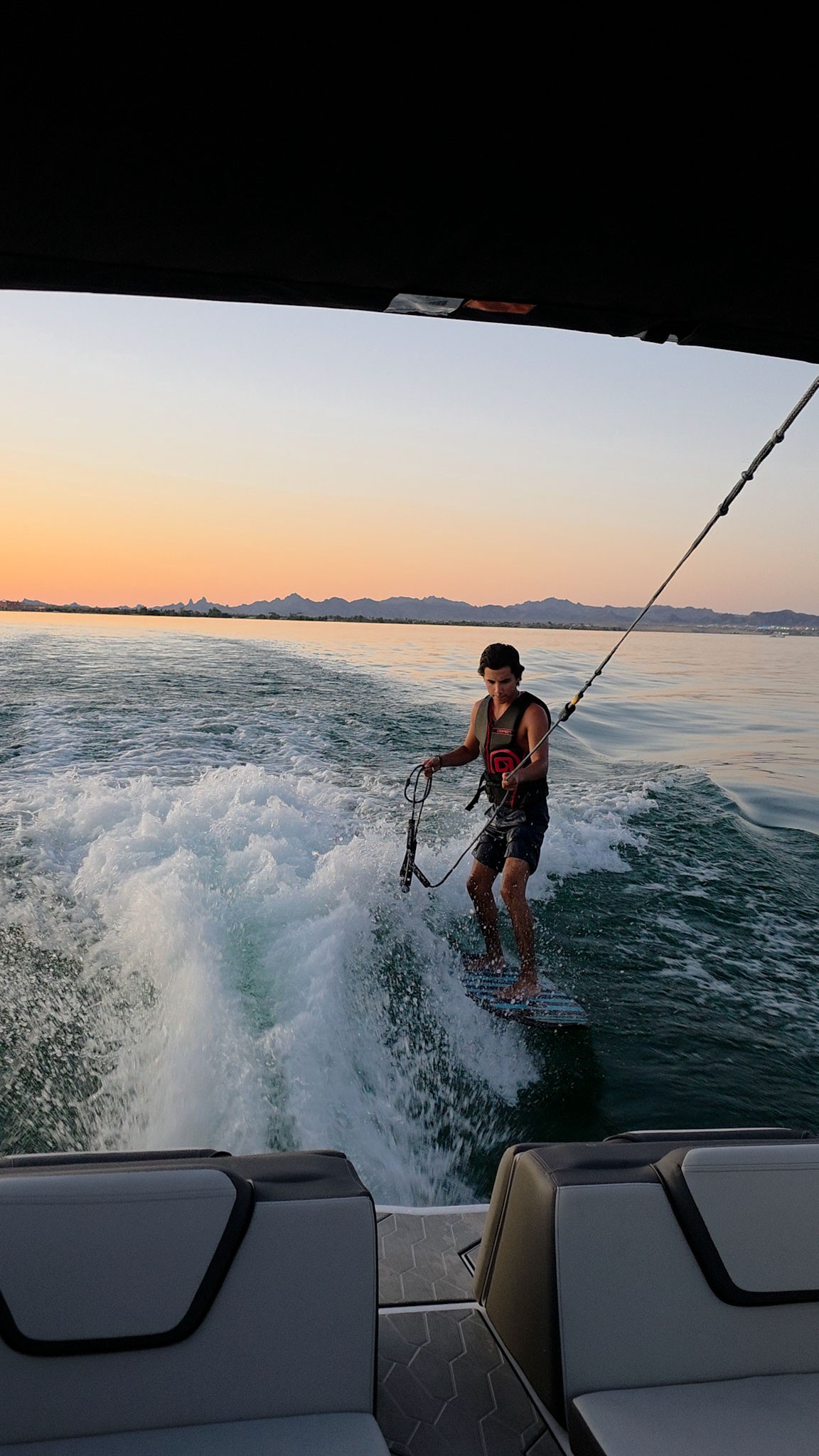 View from a boat with empty seats toward water and distant mountains at sunset.