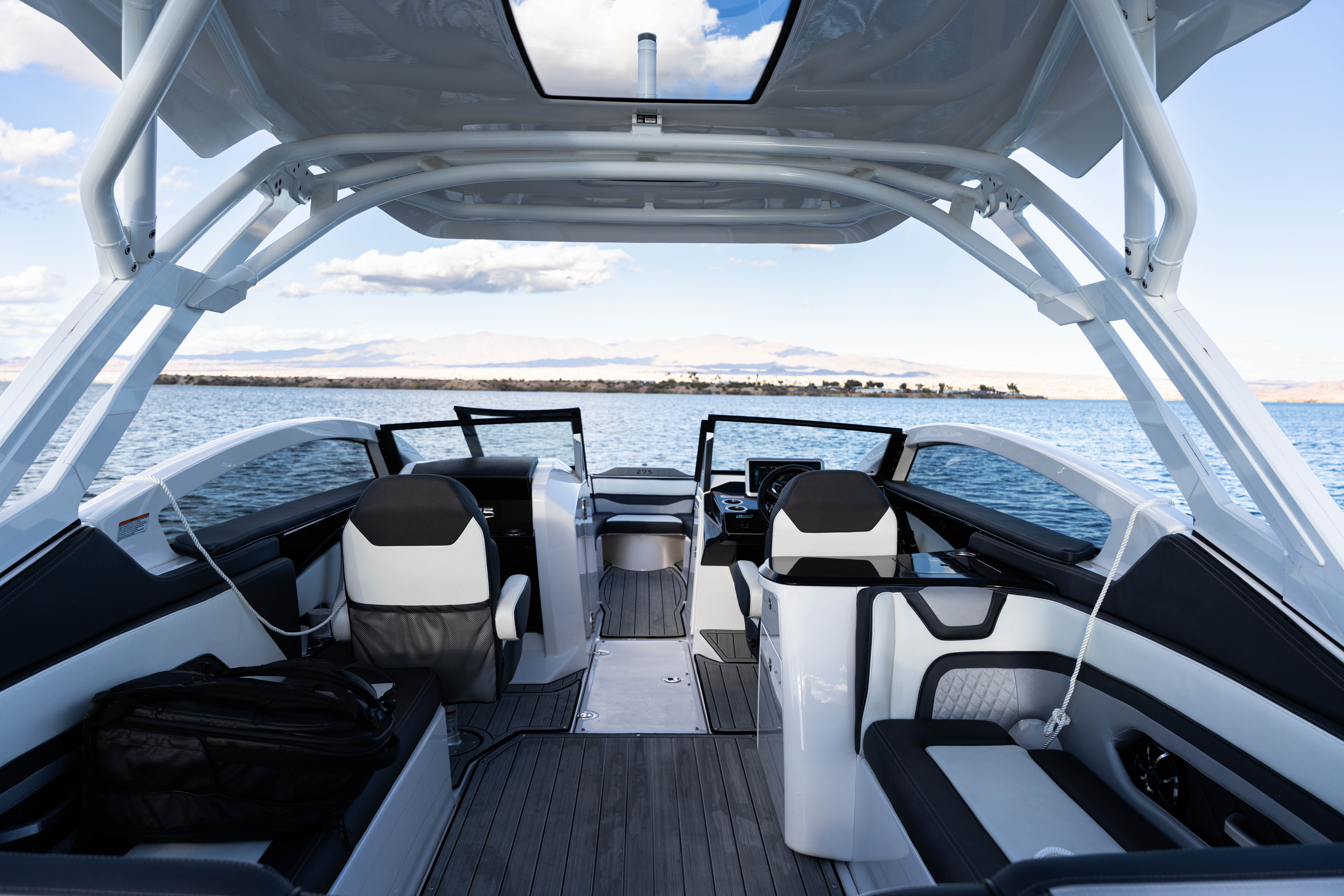 Interior deck of a modern motorboat on water with cushioned seating and a clear sky above.