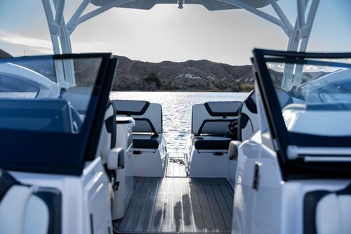 Interior view of a white boat with open windshields facing calm water and mountainous shoreline.