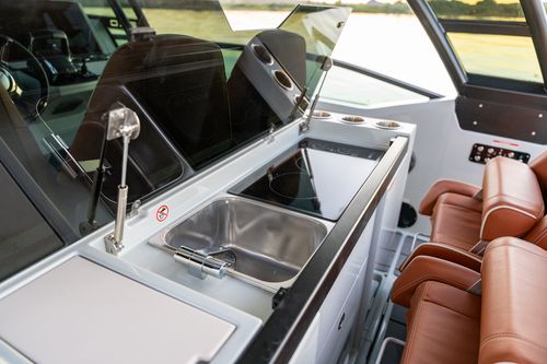 Boat interior kitchenette with stainless sink, cooktop, cup holders, and brown leather seats.