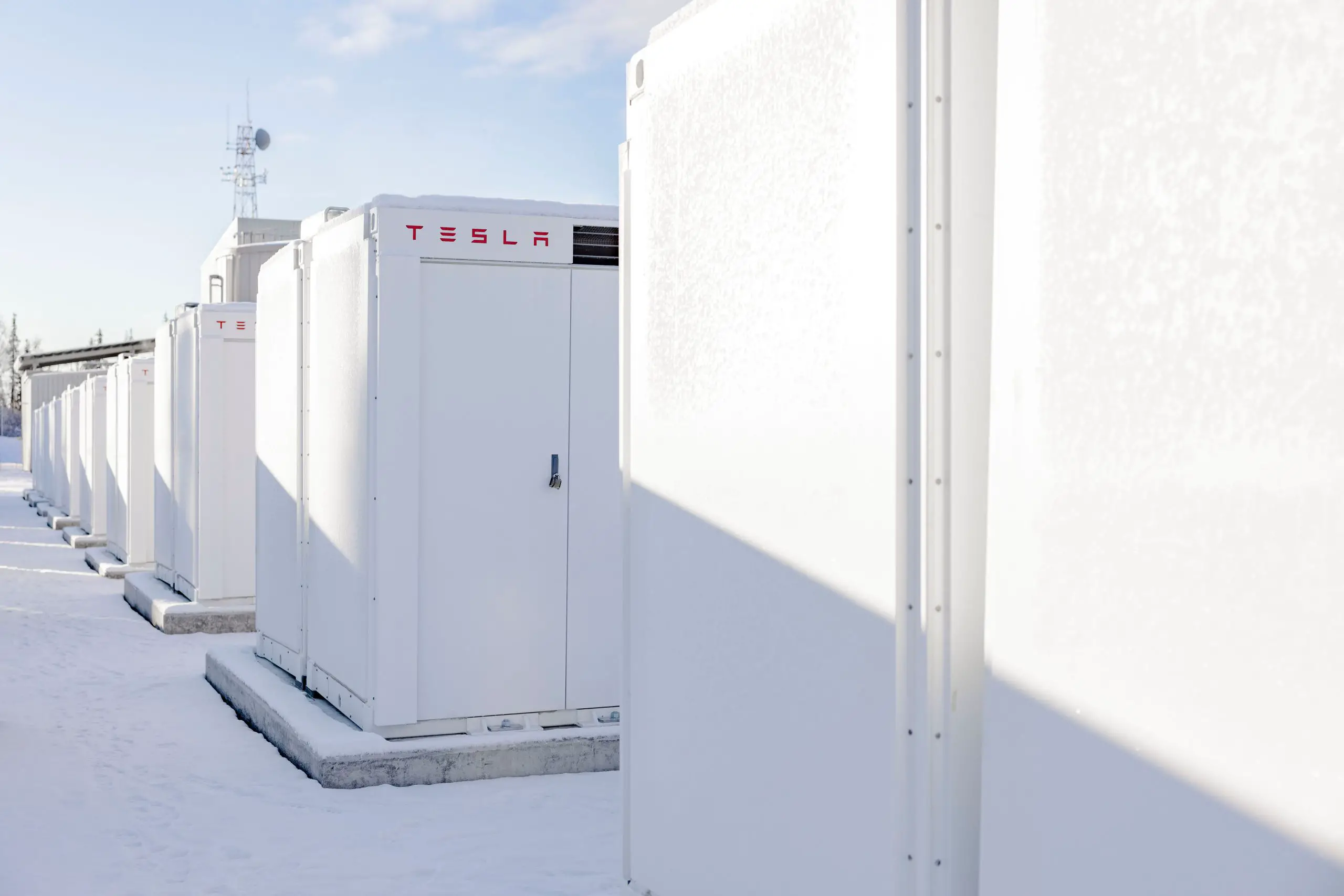 Row of white Tesla energy storage units outdoors in snow under clear sky that power Enel's systems.