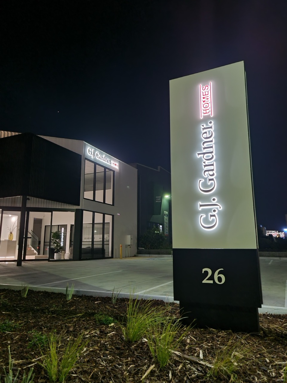 A factory roadside sign in a vertical position illuminated neon that reads GJ Gardner Homes Warragul
