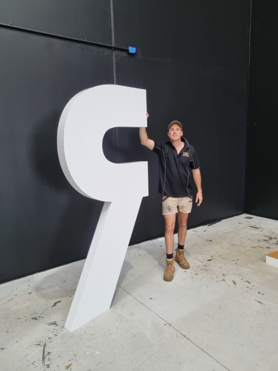 A man standing next to a large custom 3d sign of a letter R. The man is a sign writer named Michael Cox