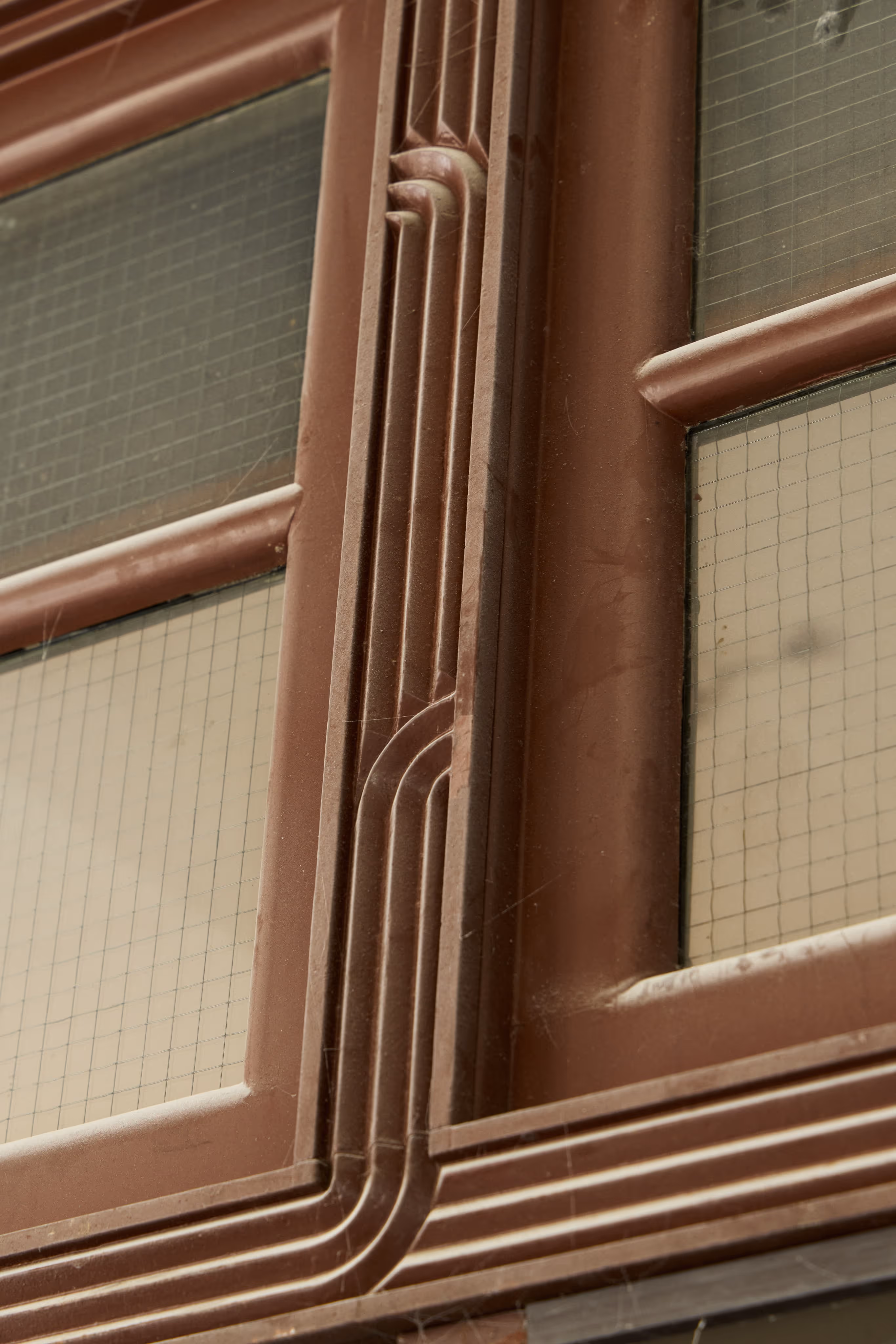 Close-up of a brown metal window frame with decorative grooves and wired glass panes.
