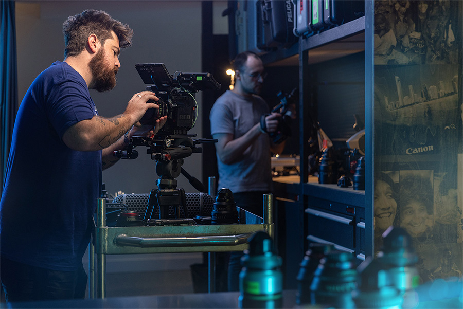 Two men adjusting professional film cameras and equipment in a dimly lit studio workspace.