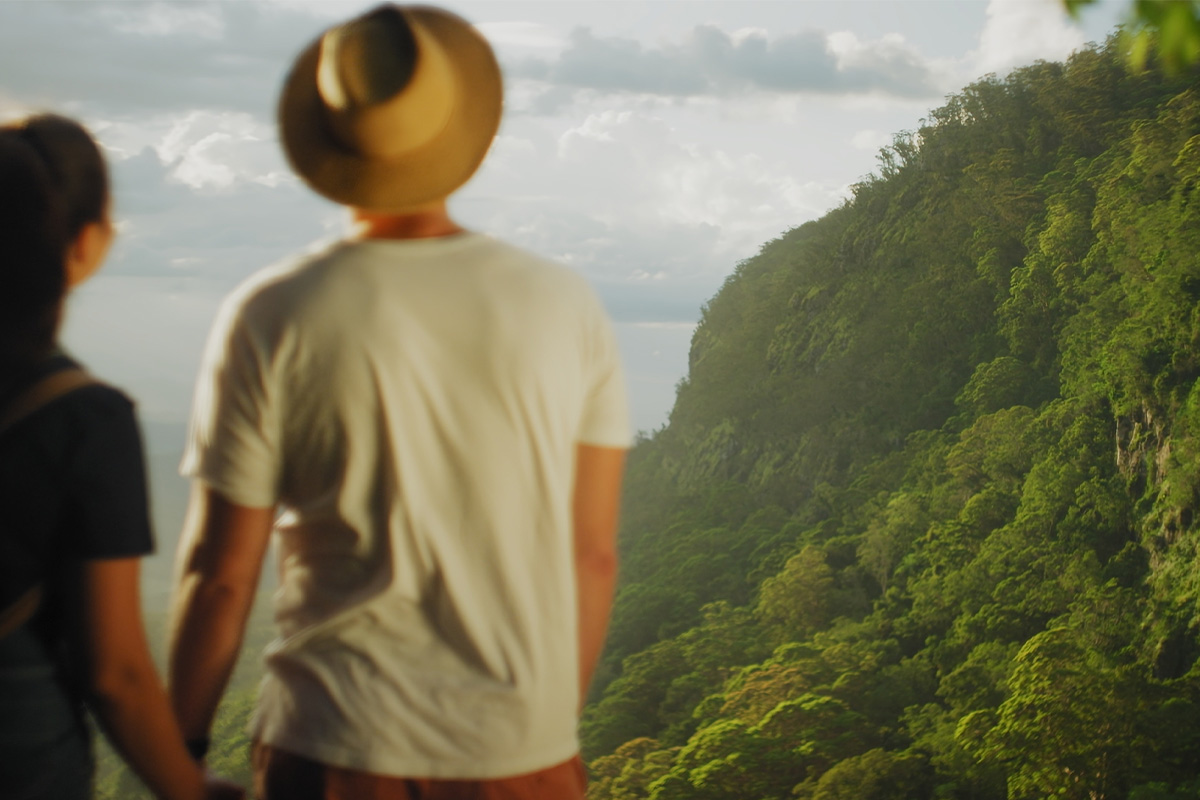Couple holding hands overlooking lush green mountains under a cloudy sky.