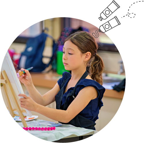 Young girl focused on painting at an easel in a classroom setting with art supplies nearby for the arts program for All Saints College in Bullcreek