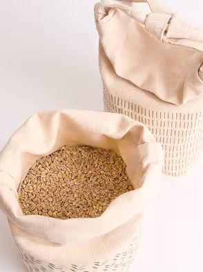 An open reusable fabric grain bag filled with grains, shown alongside a second closed bag in the background. The soft textile materials, visible contents, and minimal color palette highlight the tactile and natural qualities of the packaging system.
Photography by Tommy-Paul Keo