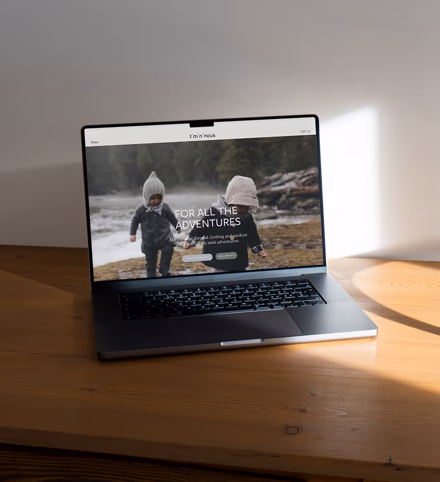 A laptop displaying the Timininous homepage placed on a wooden table beside soft natural light. The screen features two children outdoors alongside the brand’s website interface and navigation.
Mockup from Mockup.Maison