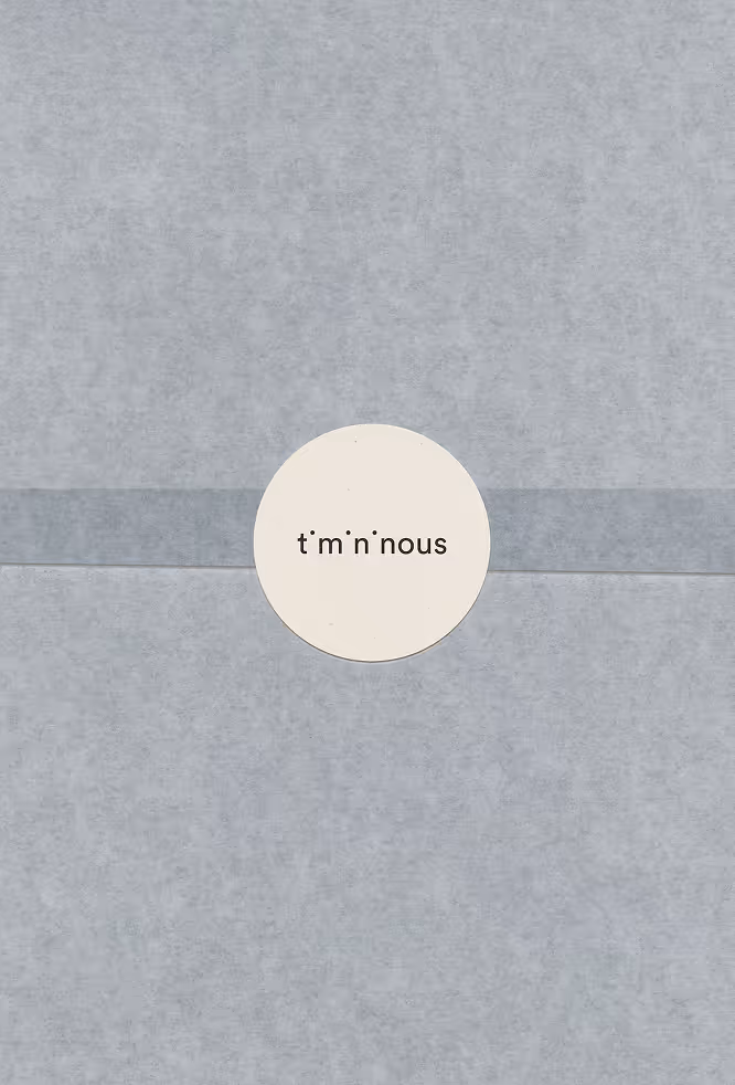A sheet of translucent wrapping paper sealed with a circular Timininous sticker placed at the center. The muted grey tones and minimal typography create a soft and understated packaging presentation.
Mockup from Bendito Mockup