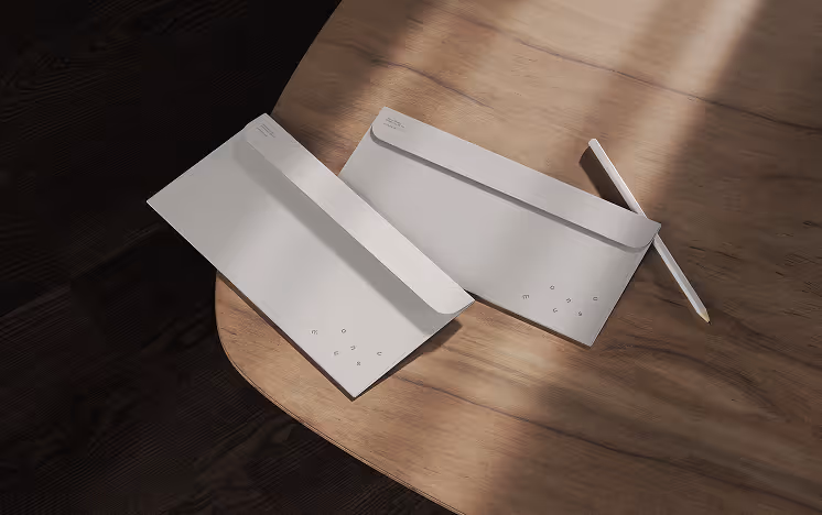 Two minimalist envelopes placed on a wooden table beside a white pencil. Soft natural shadows and subtle typography emphasize the clean and understated stationery design.
Mockup by ls.graphics