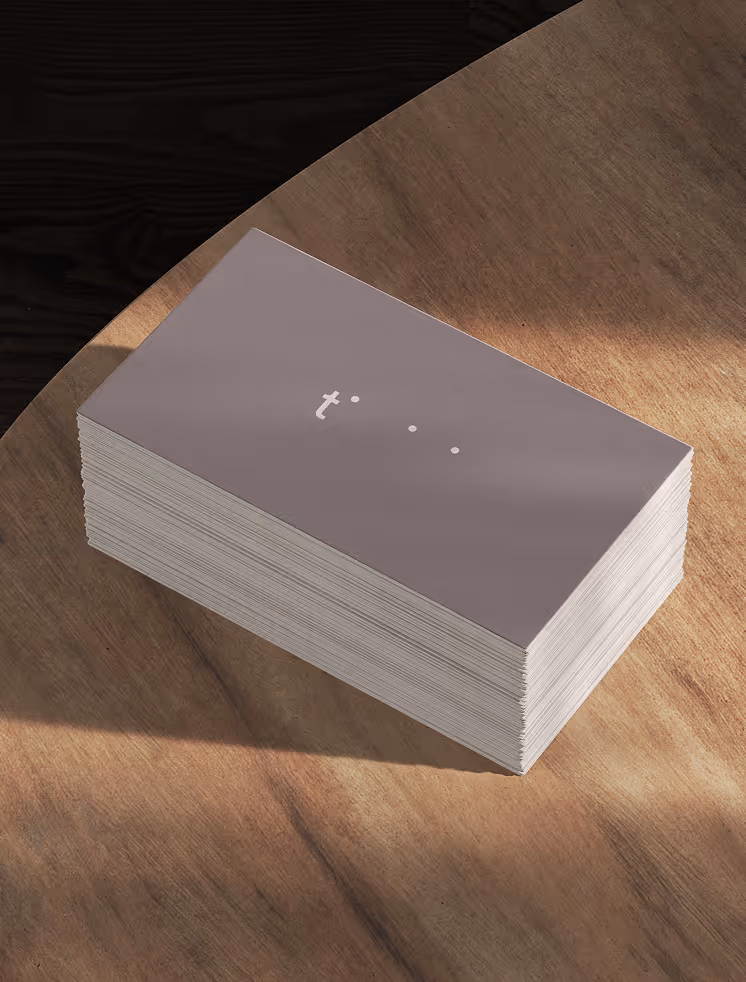 A stack of business cards placed on a wooden surface under soft directional light. The cards feature a muted colour palette and minimal typographic branding.
Mockup from ls.graphics