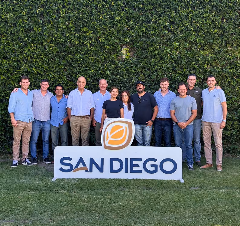 Group of 12 people standing behind a sign with SAN DIEGO in front of a green leafy wall.