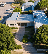 Aerial view of a modern white building surrounded by trees and a paved walkway.