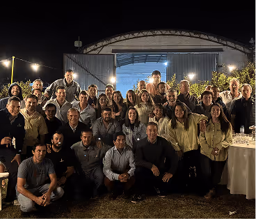 Group of about 38 people posing together outdoors at night in front of open warehouse doors.