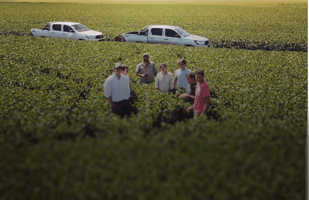 Group of seven people standing in a green field with two white pickup trucks parked in the background.
