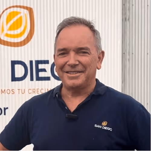 Smiling man in navy San Diego polo shirt stands in front of a white wall with a logo and text.