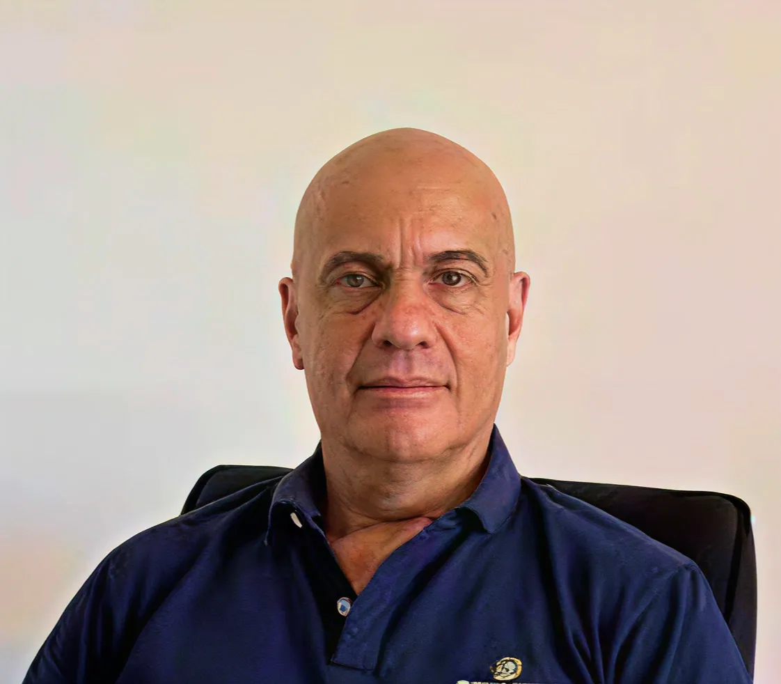 Hombre calvo de mediana edad con camisa azul posando con fondo blanco.