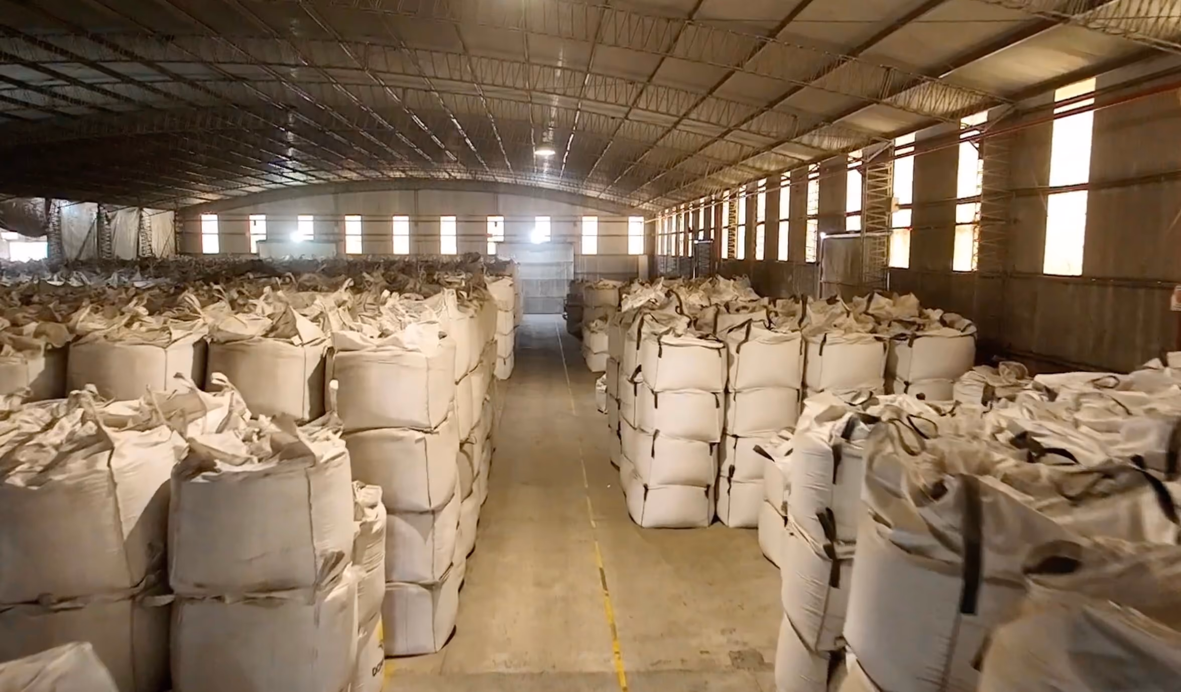 Interior de un almacén grande con pilas ordenadas de sacos industriales grandes color beige.