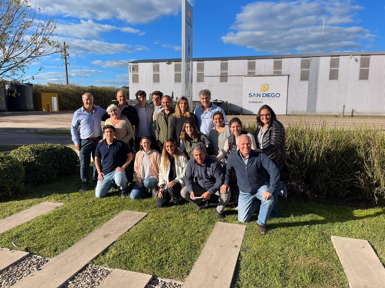 Grupo de personas posando al aire libre frente a un edificio con un cartel que dice San Diego.