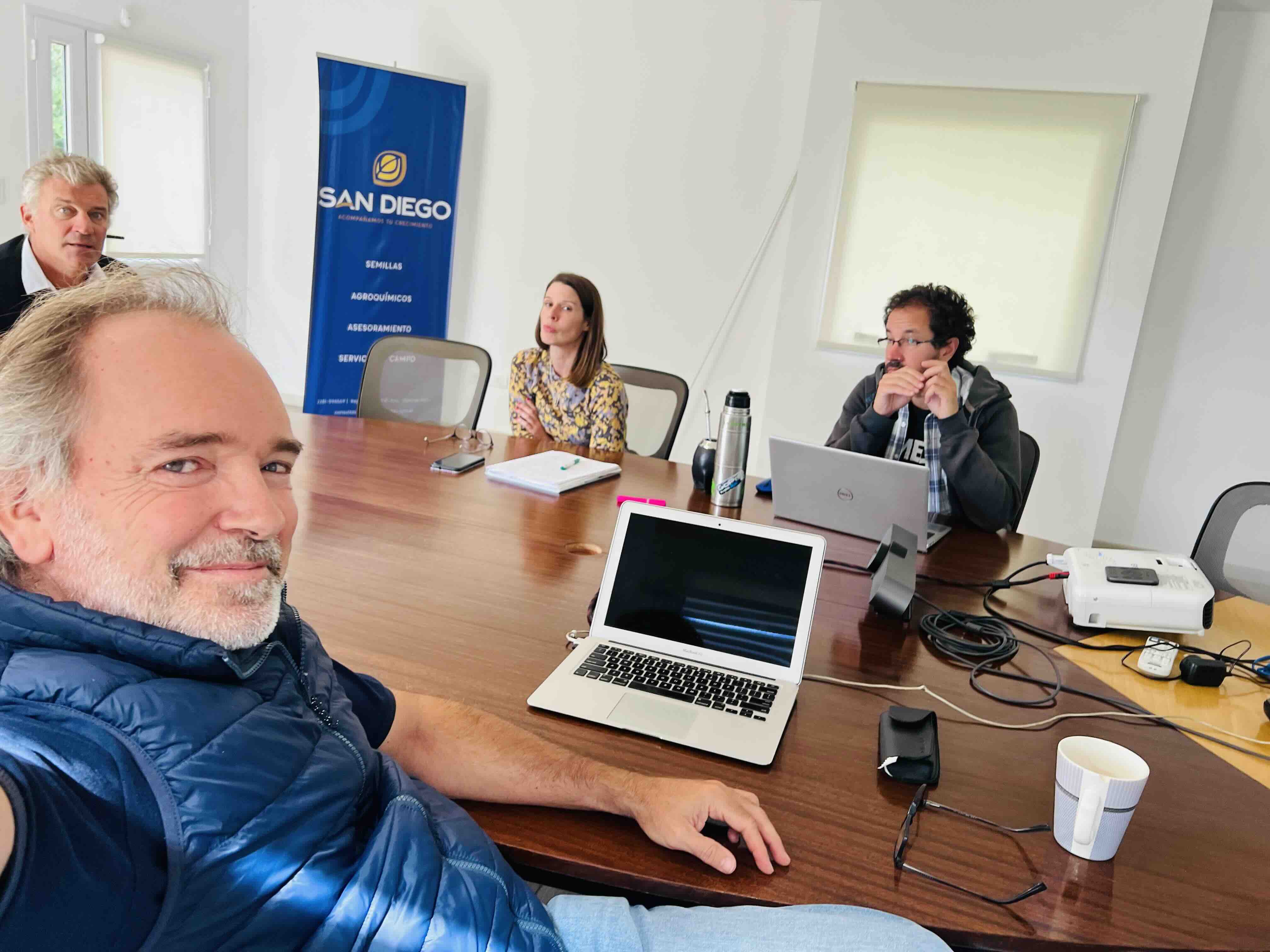 Cuatro personas reunidas alrededor de una mesa con computadoras portátiles en una oficina.