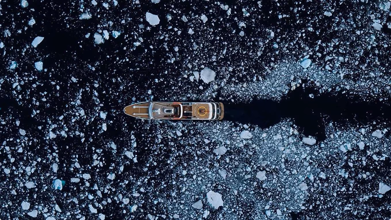 A ship cruising through dark icy waters with floating ice chunks around it.