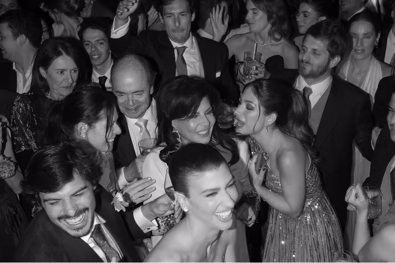 A black and white photo of a group of people dressed formally, laughing and socializing at a party.