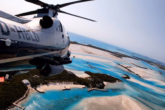 View of a helicopter flying over turquoise waters and sandy islands with docks and greenery below.