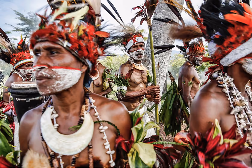 Group of indigenous men with face paint and traditional headdresses in a cultural ceremony outdoors.