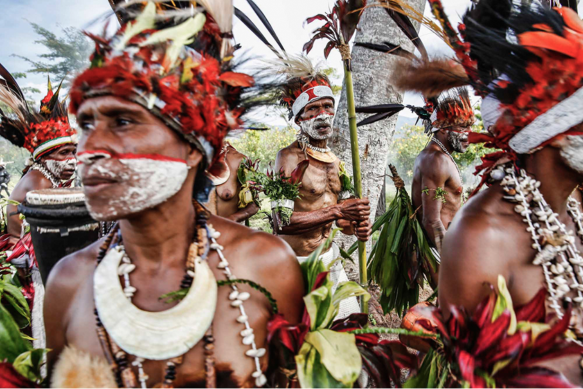 Group of indigenous men with face paint and traditional headdresses in a cultural ceremony outdoors.