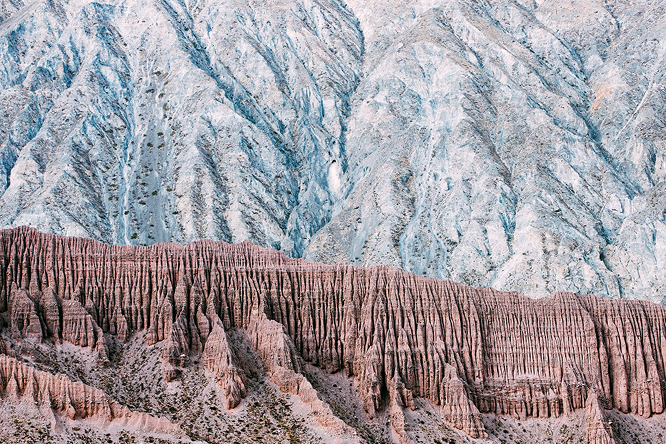Layered rock formations with vertical ridges in the foreground and rugged gray mountain slopes behind them.