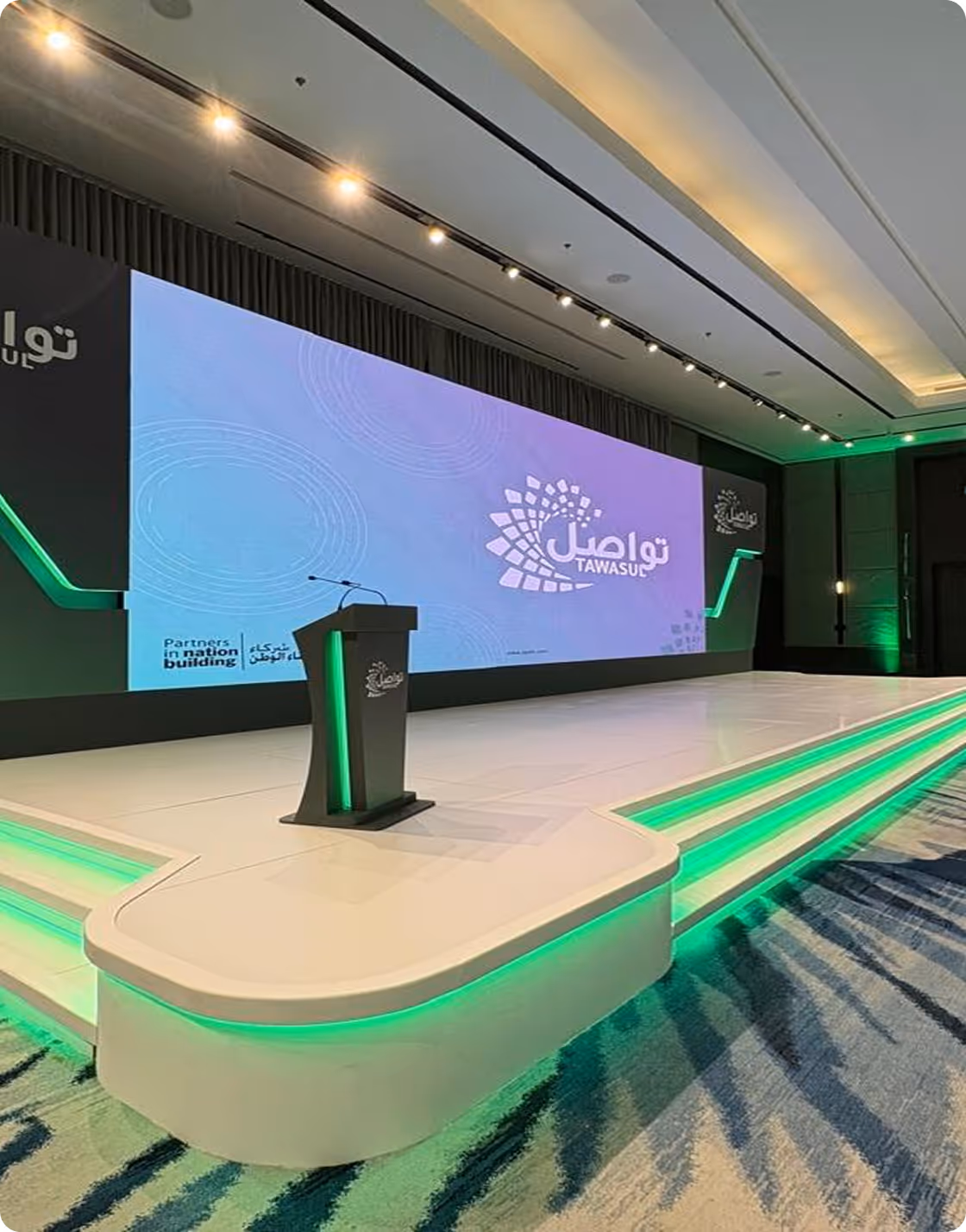 Stage with podium and large screen showing Tawasul logo and slogan Partners in Nation Building.