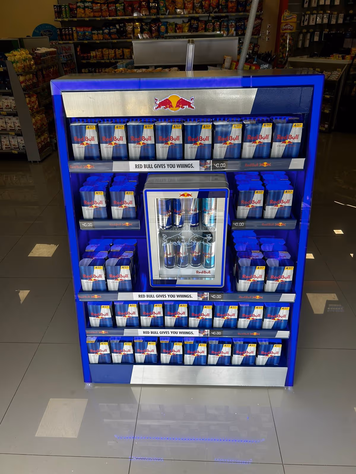 Blue display rack filled with multiple four-packs of Red Bull energy drink cans in a store.