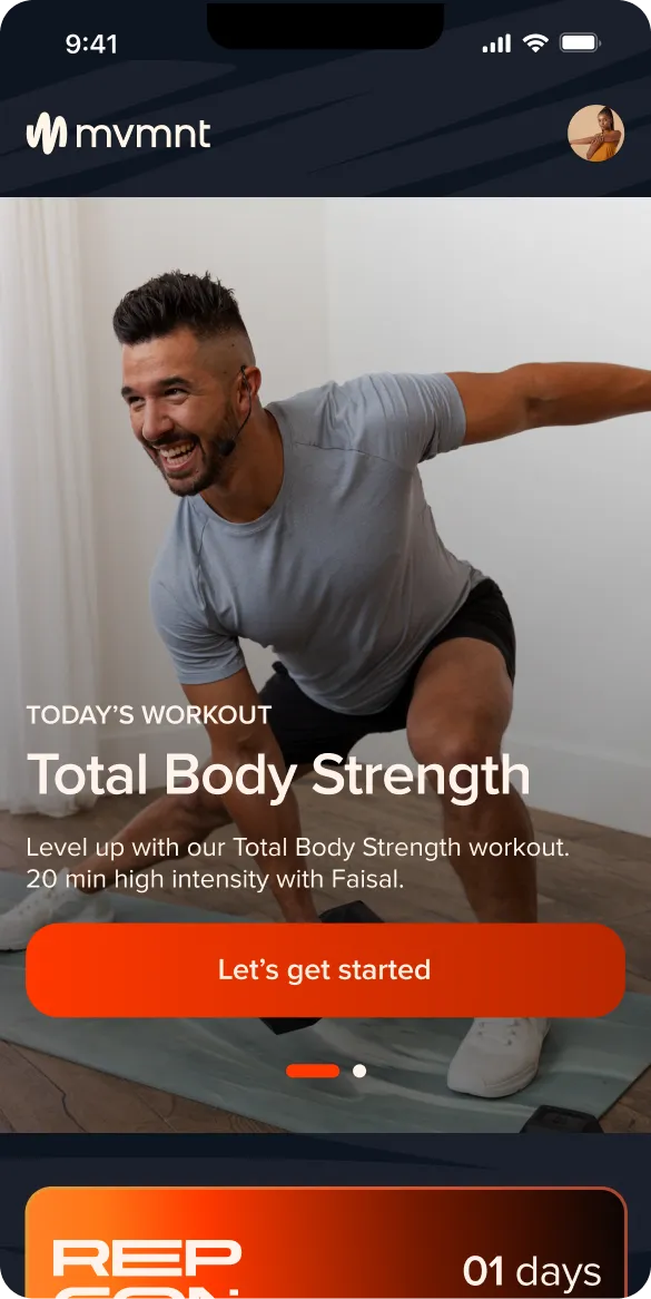 Smiling man with headset in gray shirt doing a workout stretch on a mat indoors.