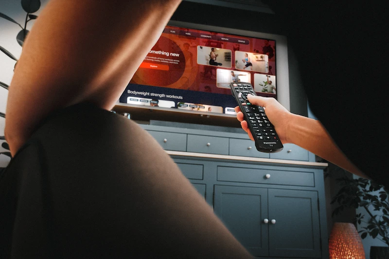 Person holding TV remote controlling workout videos displayed on a mounted television screen.