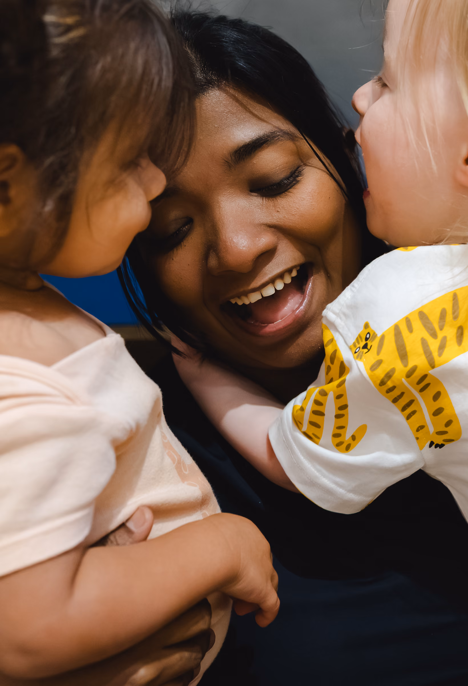 Smiling woman interacting closely with two young children, one wearing a shirt with yellow tiger print.