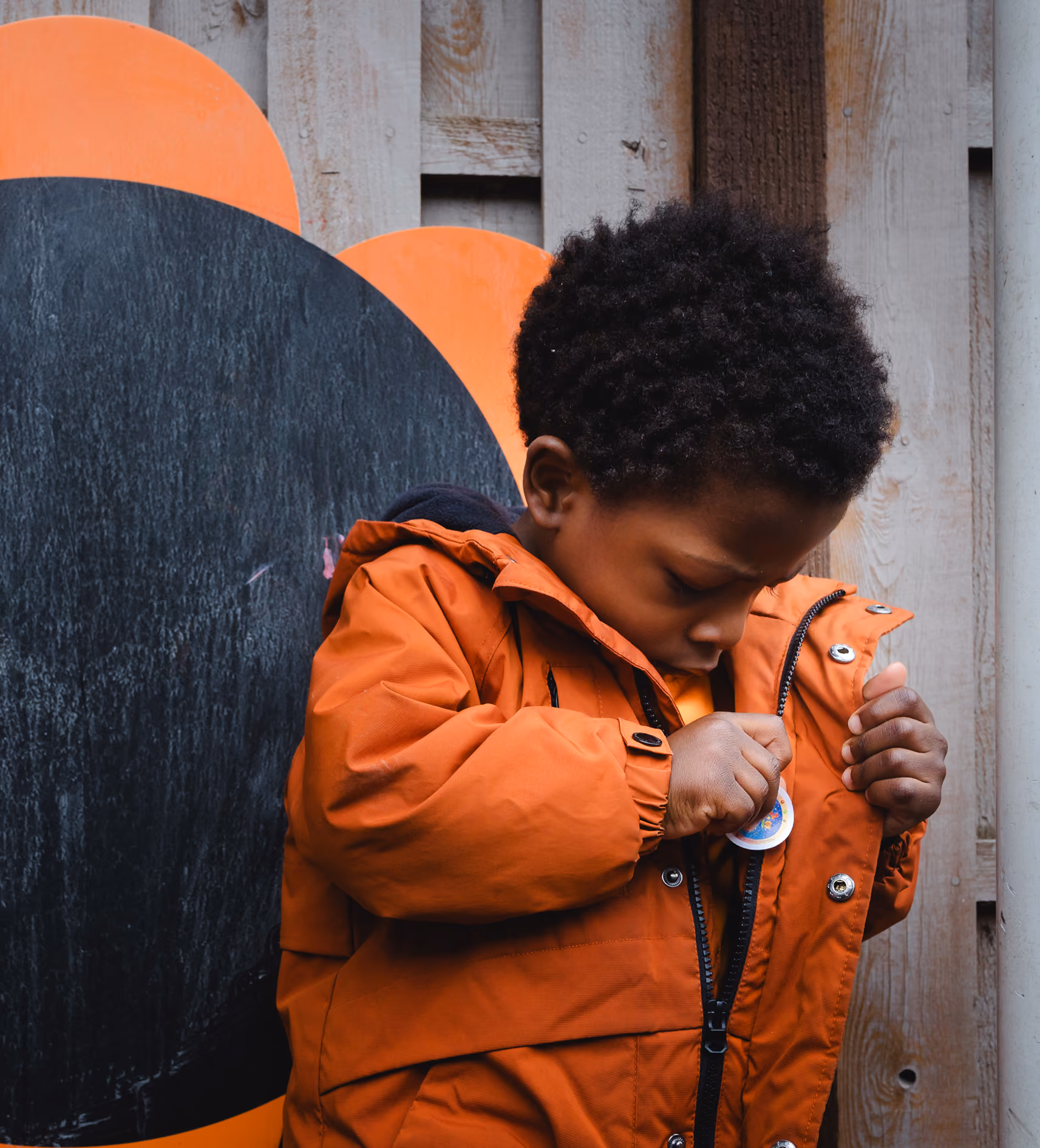 Young boy in an orange jacket looking down while adjusting a pin on the jacket.