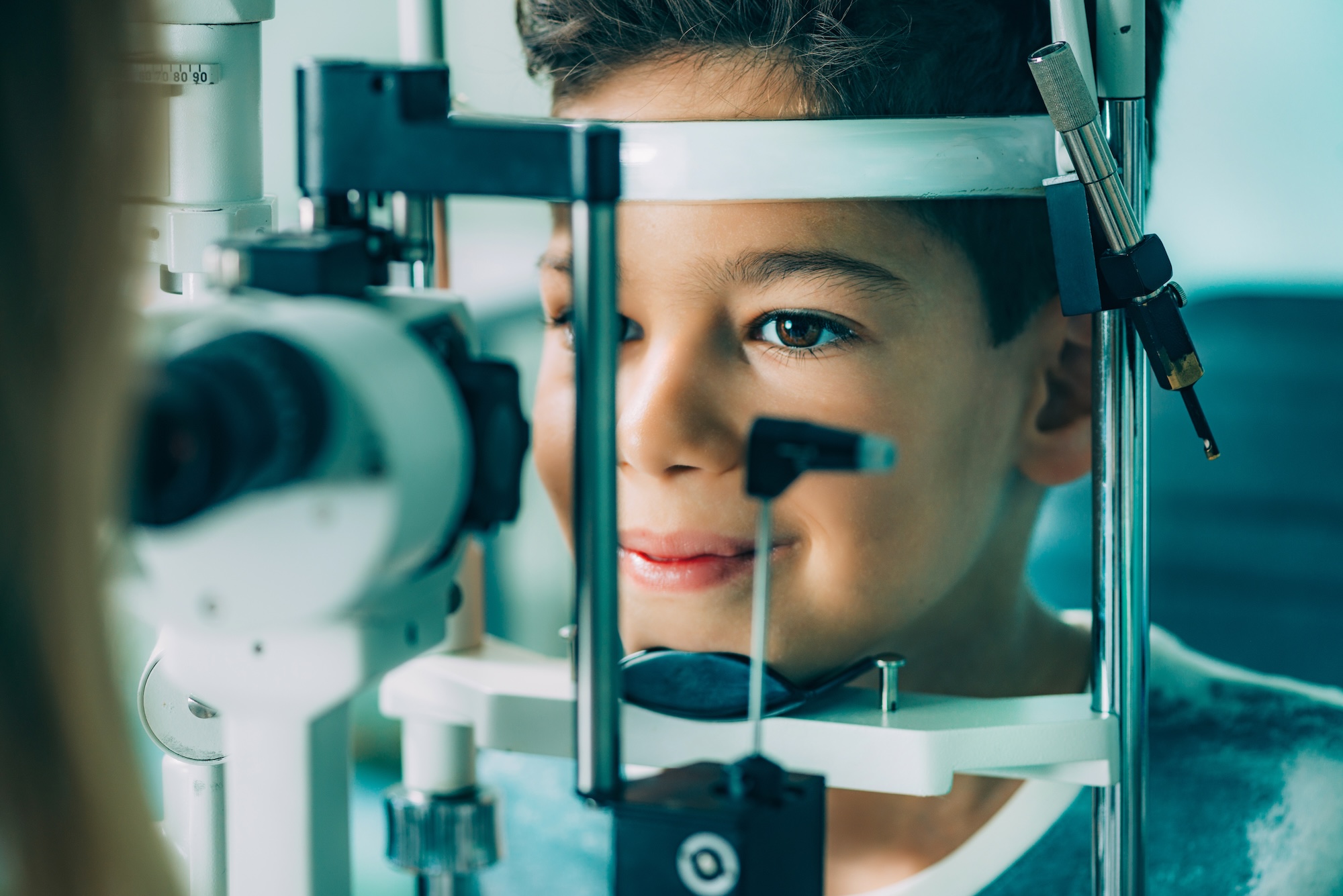 Young boy undergoing an eye exam using a slit lamp at an optometrist's office.
