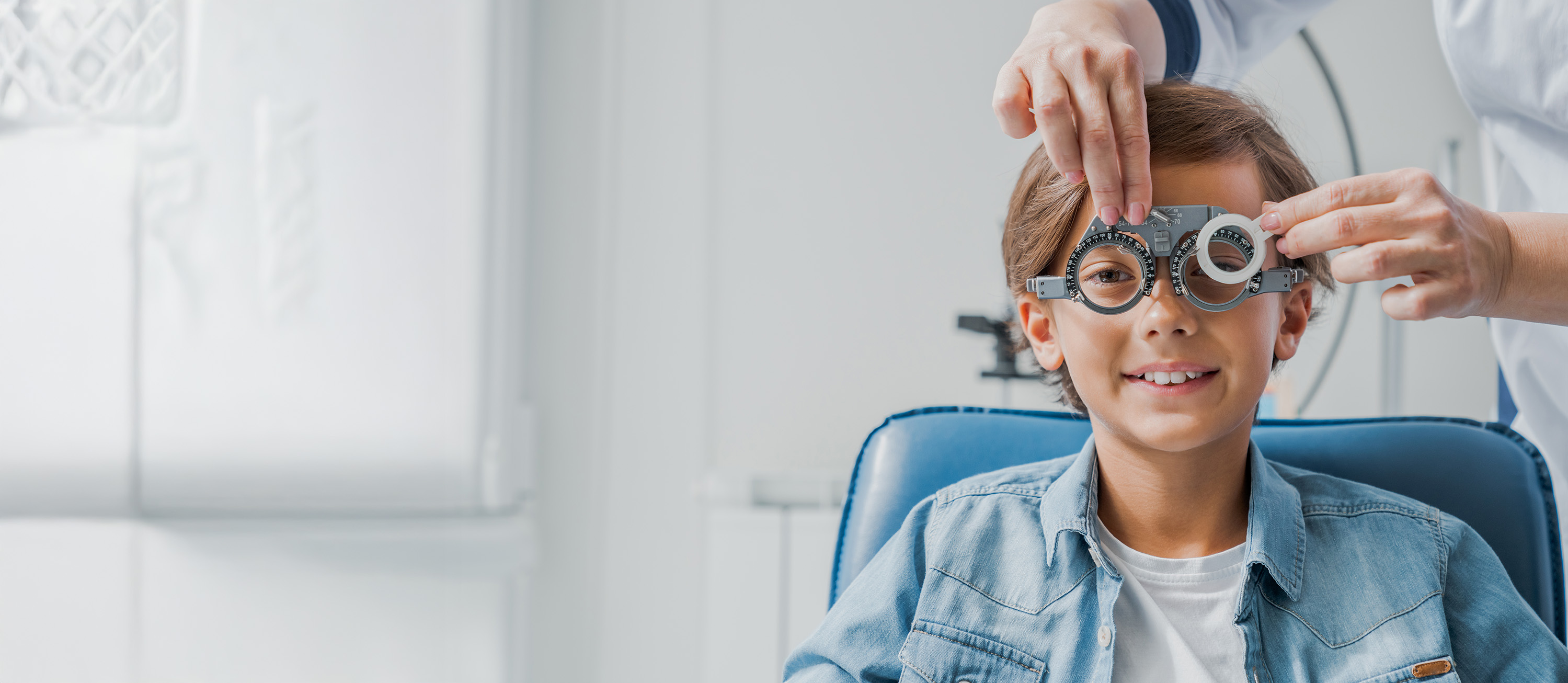Child smiling while an eye doctor adjusts a phoropter during an eye exam.