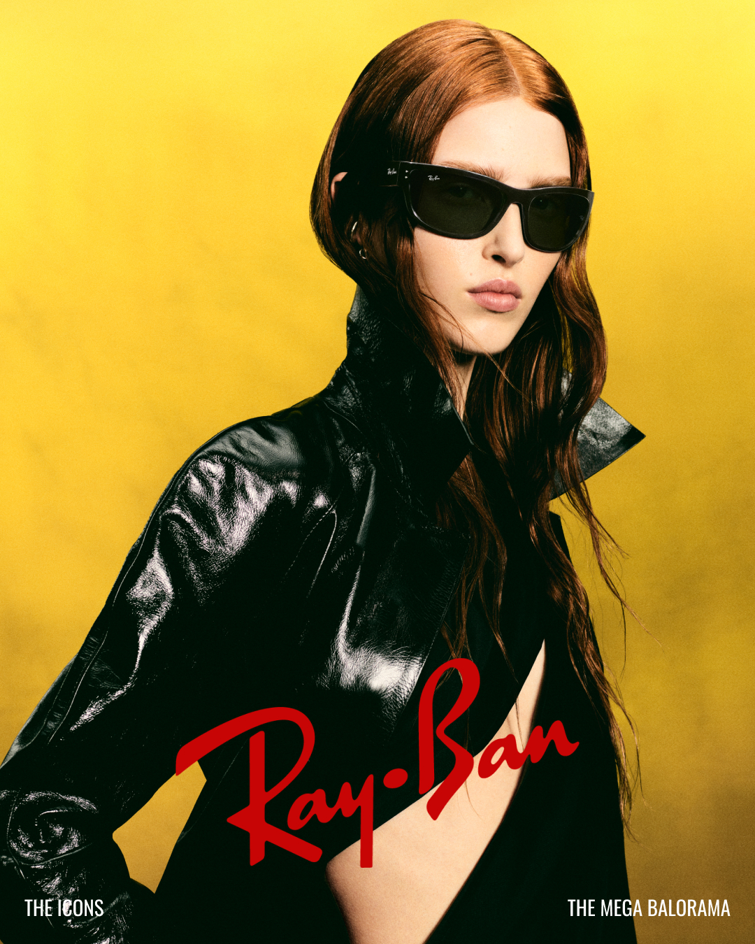 Woman with long red hair wearing black Ray-Ban sunglasses and a shiny black jacket on yellow background.