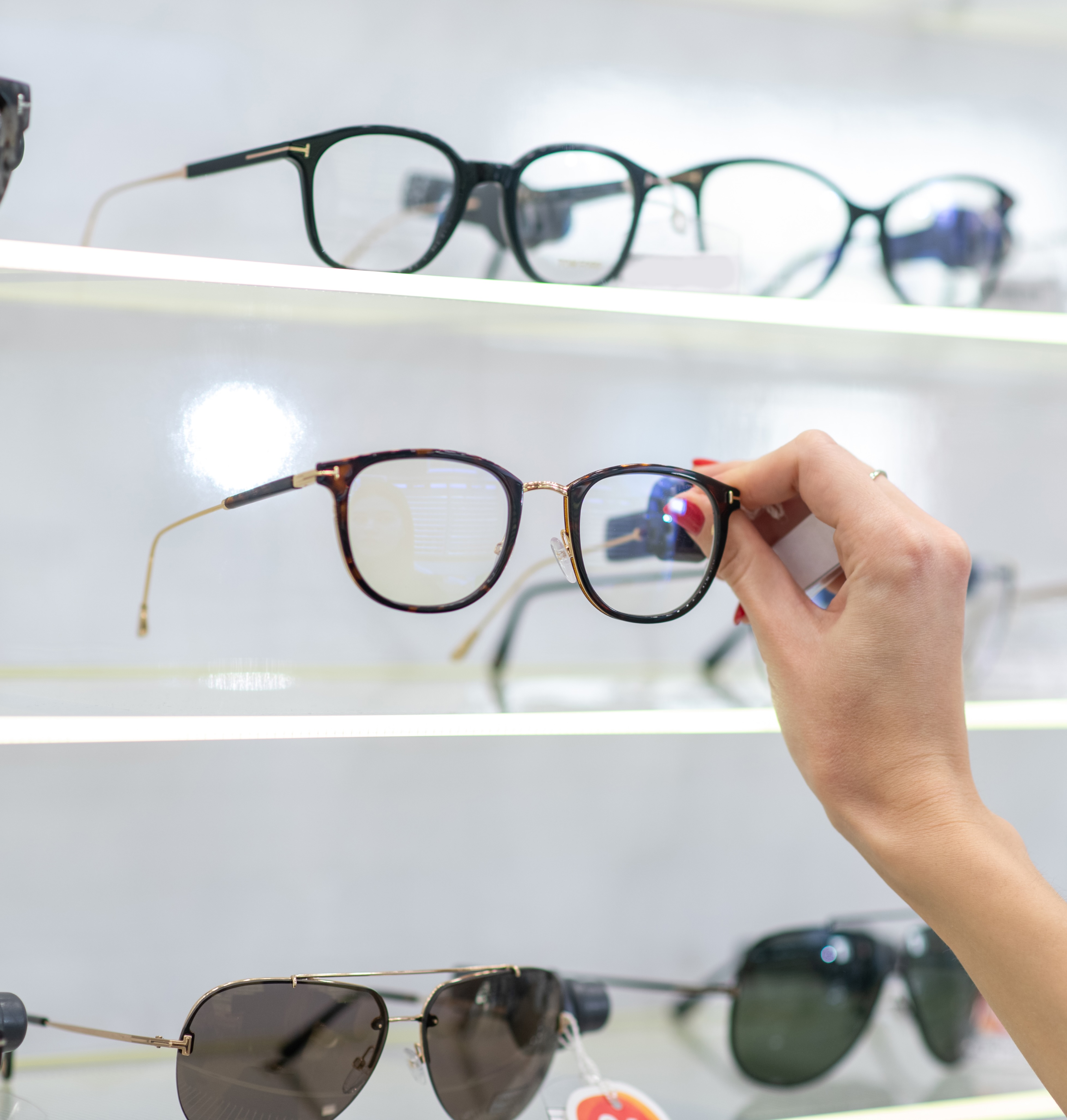 Hand holding a pair of eyeglasses with tortoiseshell frames at an optical store display.