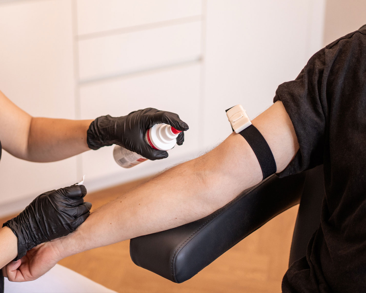 Medizinische Fachkraft trägt Handschuhe und bereitet den Arm eines Patienten mit einem Sprühmittel vor.