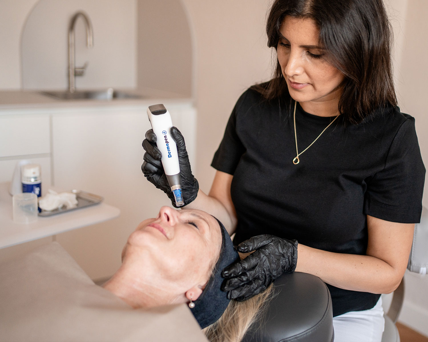 Kosmetikerin mit Handschuhen führt Microneedling mit Dermapen bei einer Frau durch, die entspannt liegt.