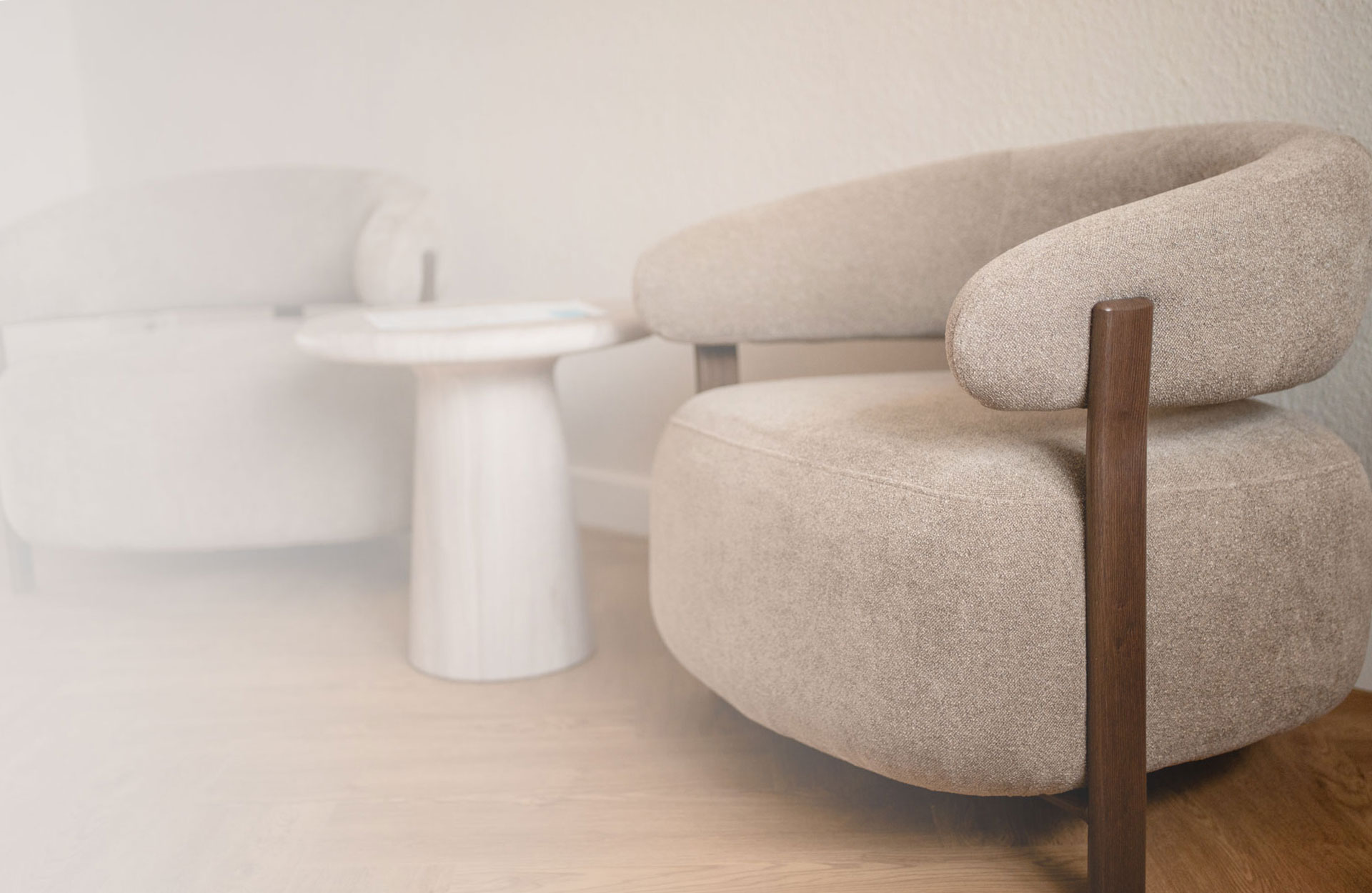 Beiger Polstersessel mit braunen Holzbeinen und kleinem weißem Beistelltisch im Hintergrund.