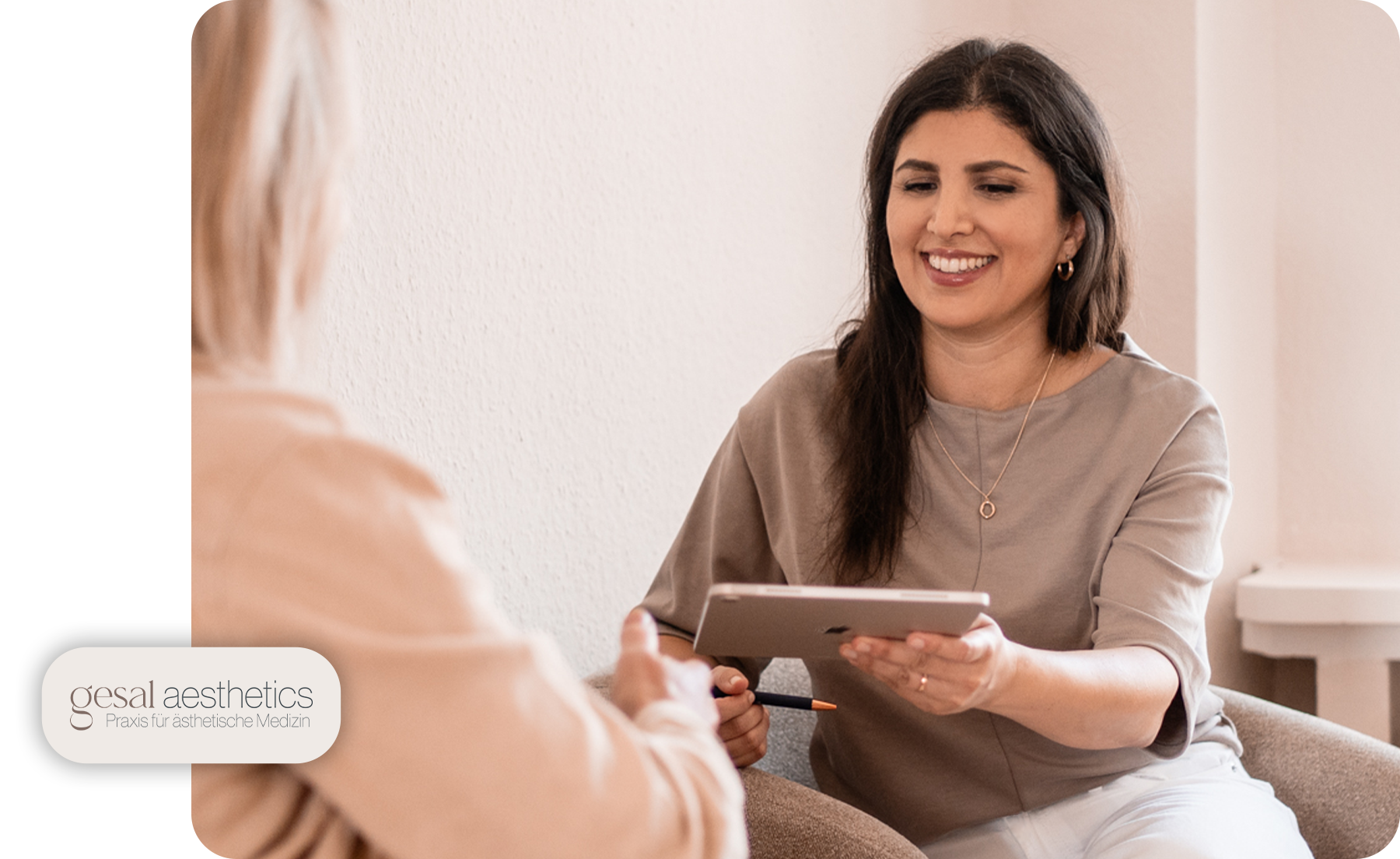 Frau lächelt und zeigt einem Patienten auf einem Tablet medizinische Informationen.