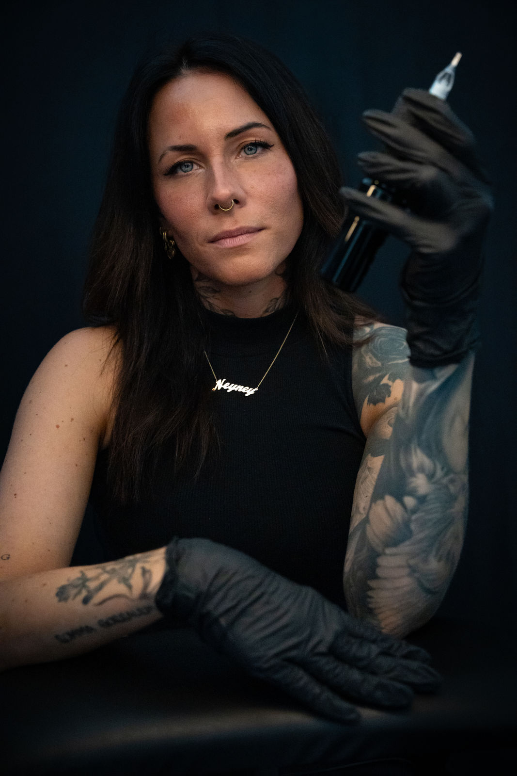 tattoo Artist mit schwarzen Handschuhen und Tattoos hält eine Tätowiermaschine in der Hand. Angebot von Frackles möglich.