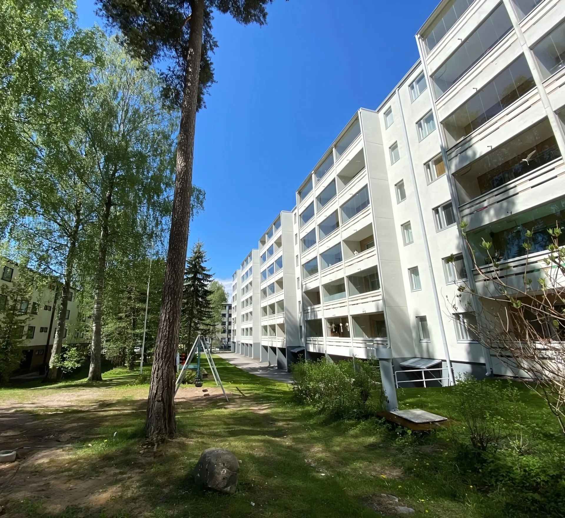 Linjasaneerattu kerrostalo ja sen piha-alue kesällä.