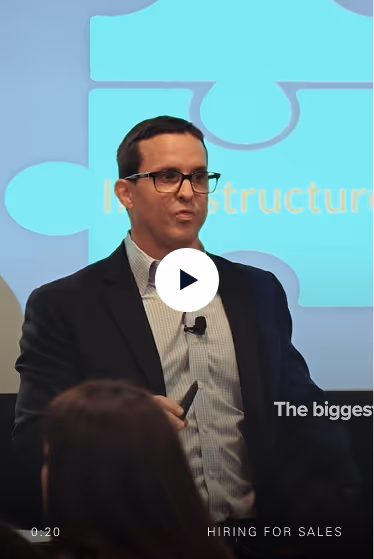 Man in glasses and suit giving a presentation on sales with puzzle piece graphic behind him.