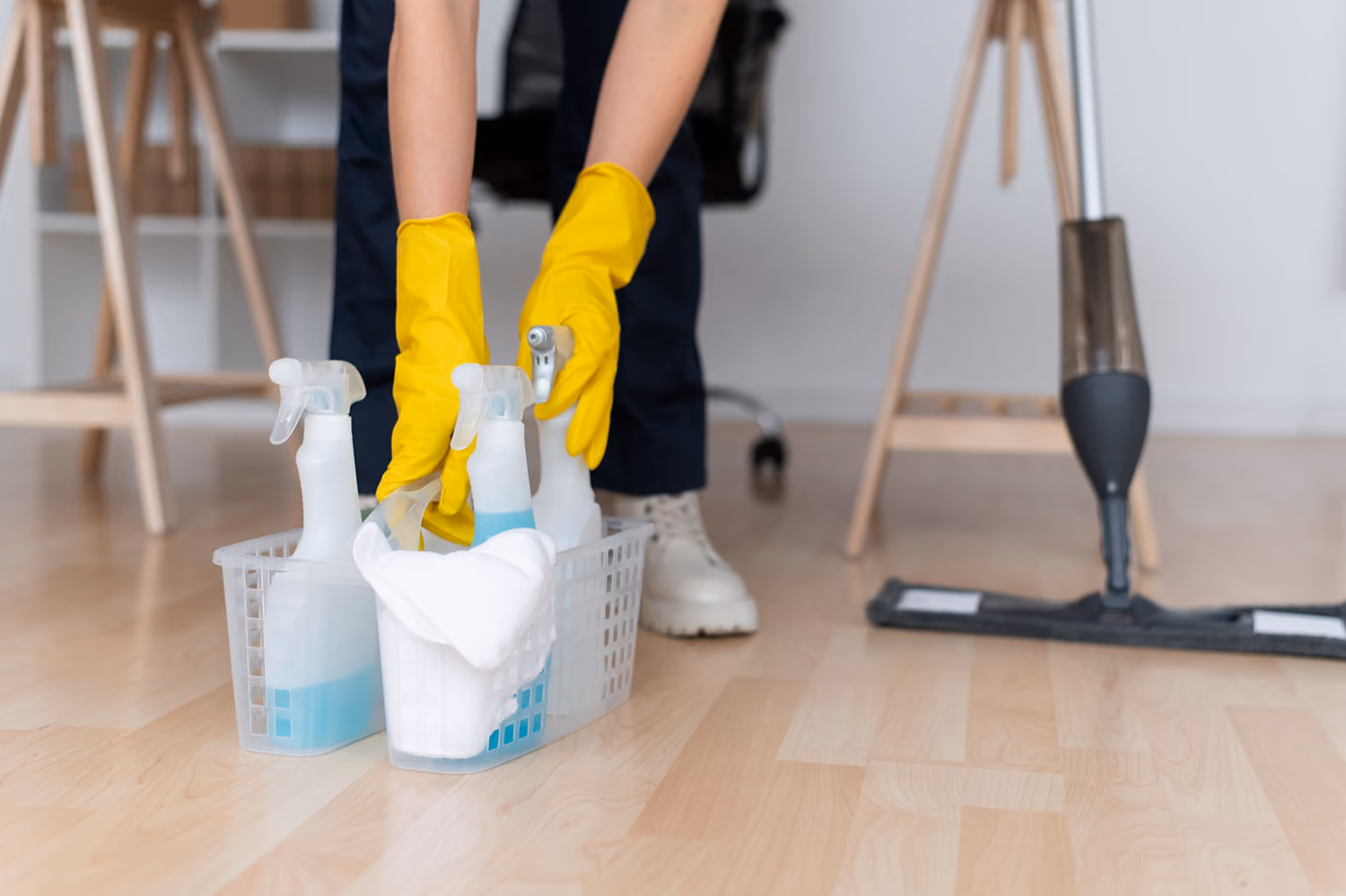 Reinigung nach Umbau- und Renovierungsarbeiten: Reinigungskraft in Firmenkleidung reinigt den Boden in einem Raum; daneben steht ein Korb mit Reinigungszubehör, Reinigungsmitteln und Sprühflaschen, separat steht ein Staubsauger.