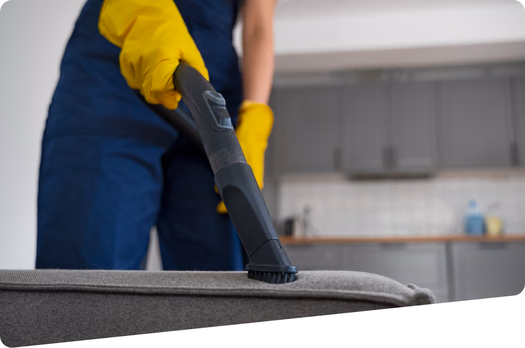 Grund- und Sonderreinigung: Reinigungskraft in Firmenkleidung reinigt Polstermöbel mit einem speziellen Gerät.